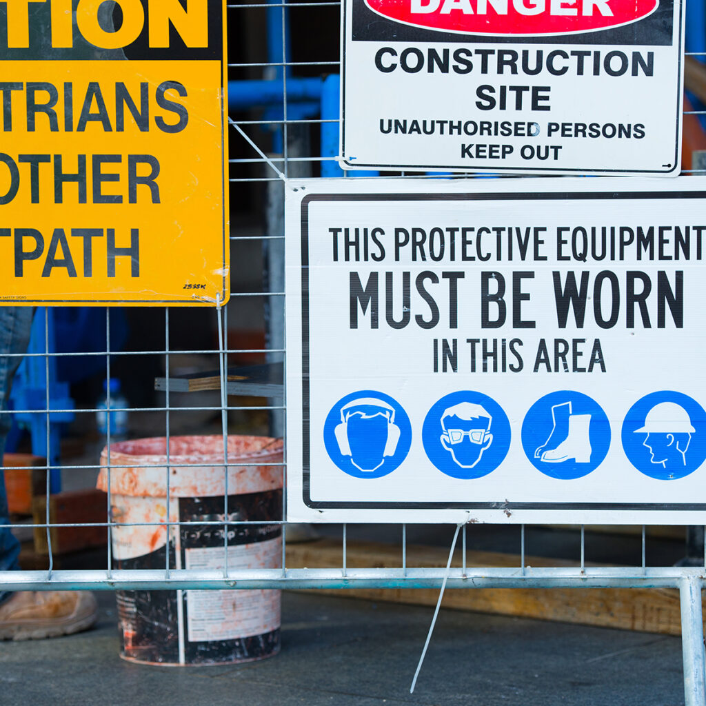 Construction site safety sign listing required protective equipment with blue PPE icons