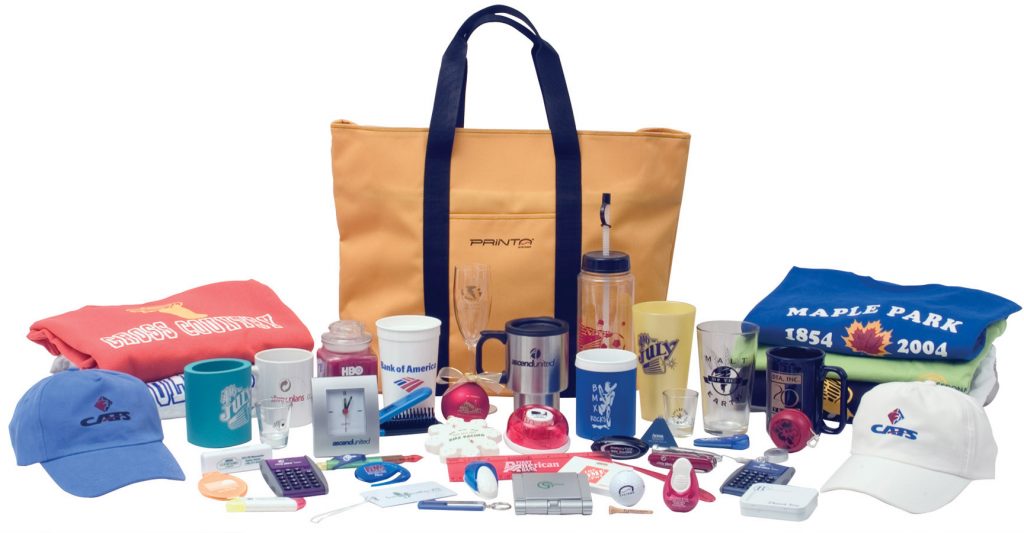 Assorted custom-printed Promotional Products including tote bag, mugs, tumblers, t-shirts, and caps displayed together.