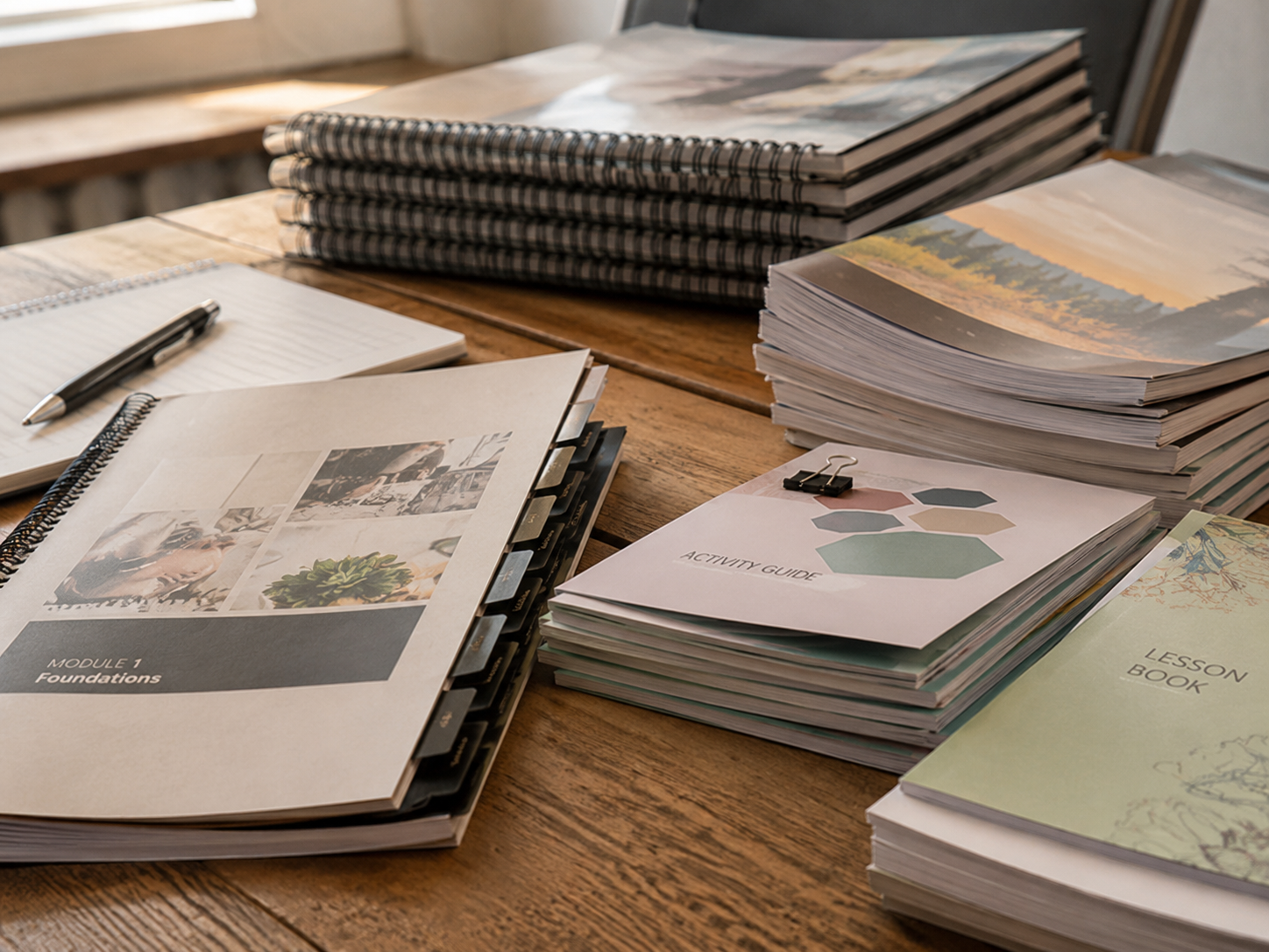 Printed course manuals, workbooks, lesson books, and activity guides arranged on a table
